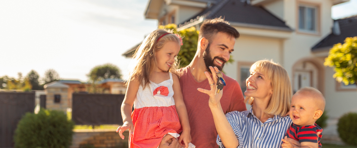Happy family with two children holding house keys while standing in front of their new home
