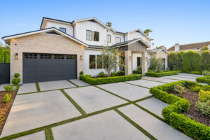 Modern two-story white farmhouse with light stone accents, a dark gray garage, and a contemporary concrete grid driveway with grass strips.