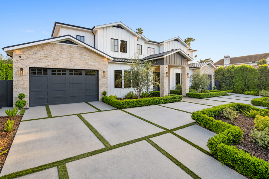 Modern two-story white farmhouse with light stone accents, a dark gray garage, and a contemporary concrete grid driveway with grass strips.